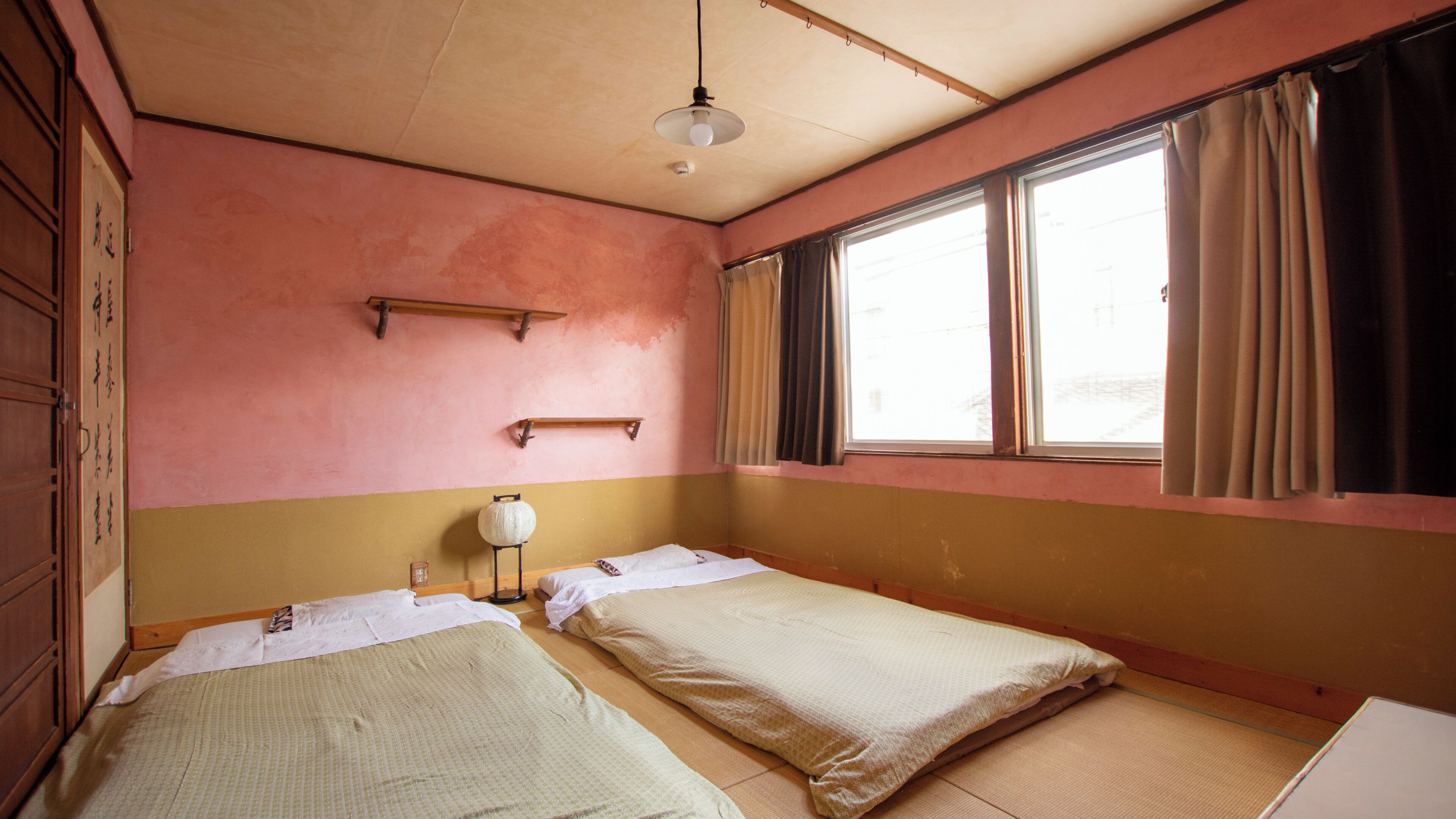 Habitació amb dos llits, una prestatgeria, una làmpada penjant i una finestra amb cortines.