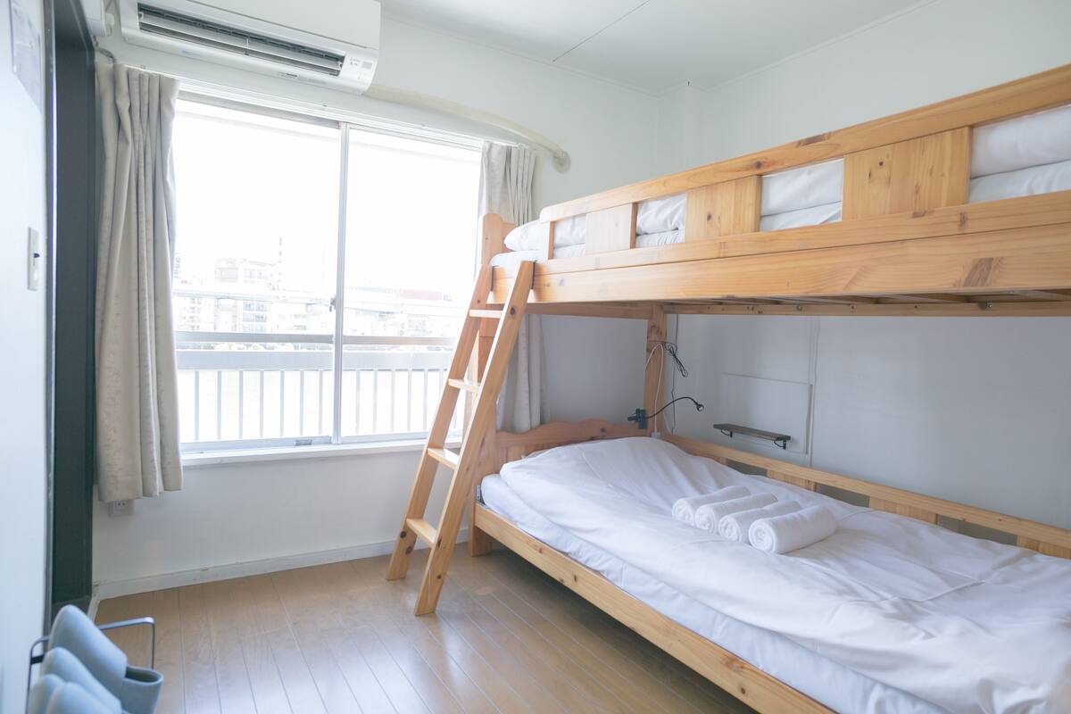 Dormitorio con literas, una escalera de madera, ropa de cama blanca y una ventana con cortinas.