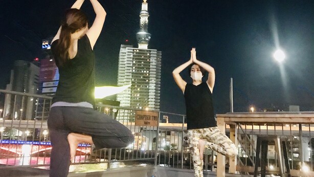 Two people practicing yoga on a rooftop with a cityscape and a tower in the background. - Hostel Chapter Two Tokyo (Tokyo)