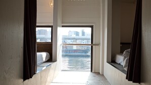 A narrow room with a view of a waterway and buildings. There are two beds with curtains. - Hostel Chapter Two Tokyo (Tokyo)