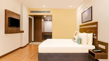 Habitación de hotel con cama, televisión montada en la pared, mesita de noche con teléfono y un cuadro en la pared.