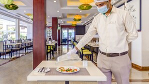 A hotel dining area with tables, chairs, and a waiter serving food.