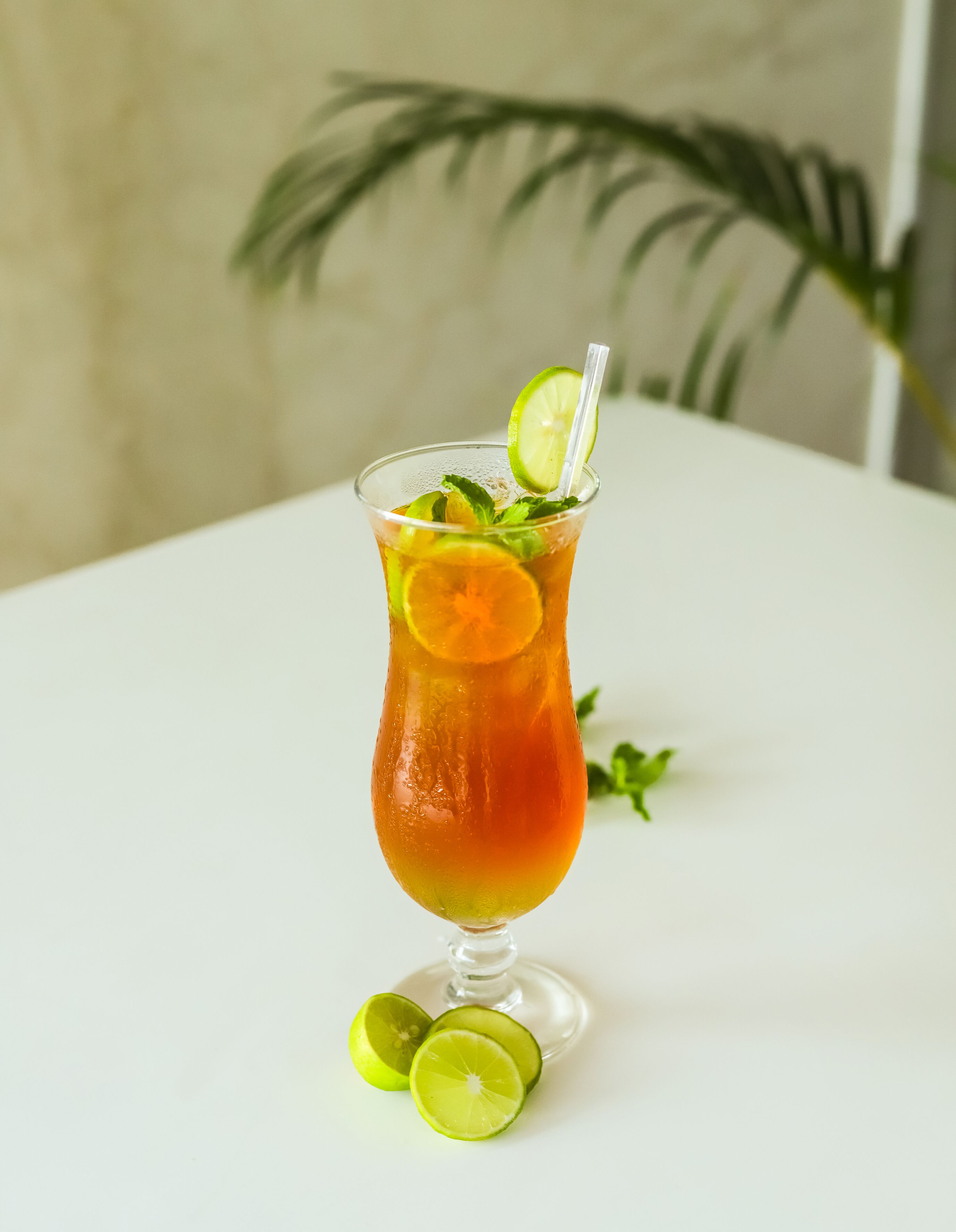 A clear glass with a lime slice and mint garnish on a white table.