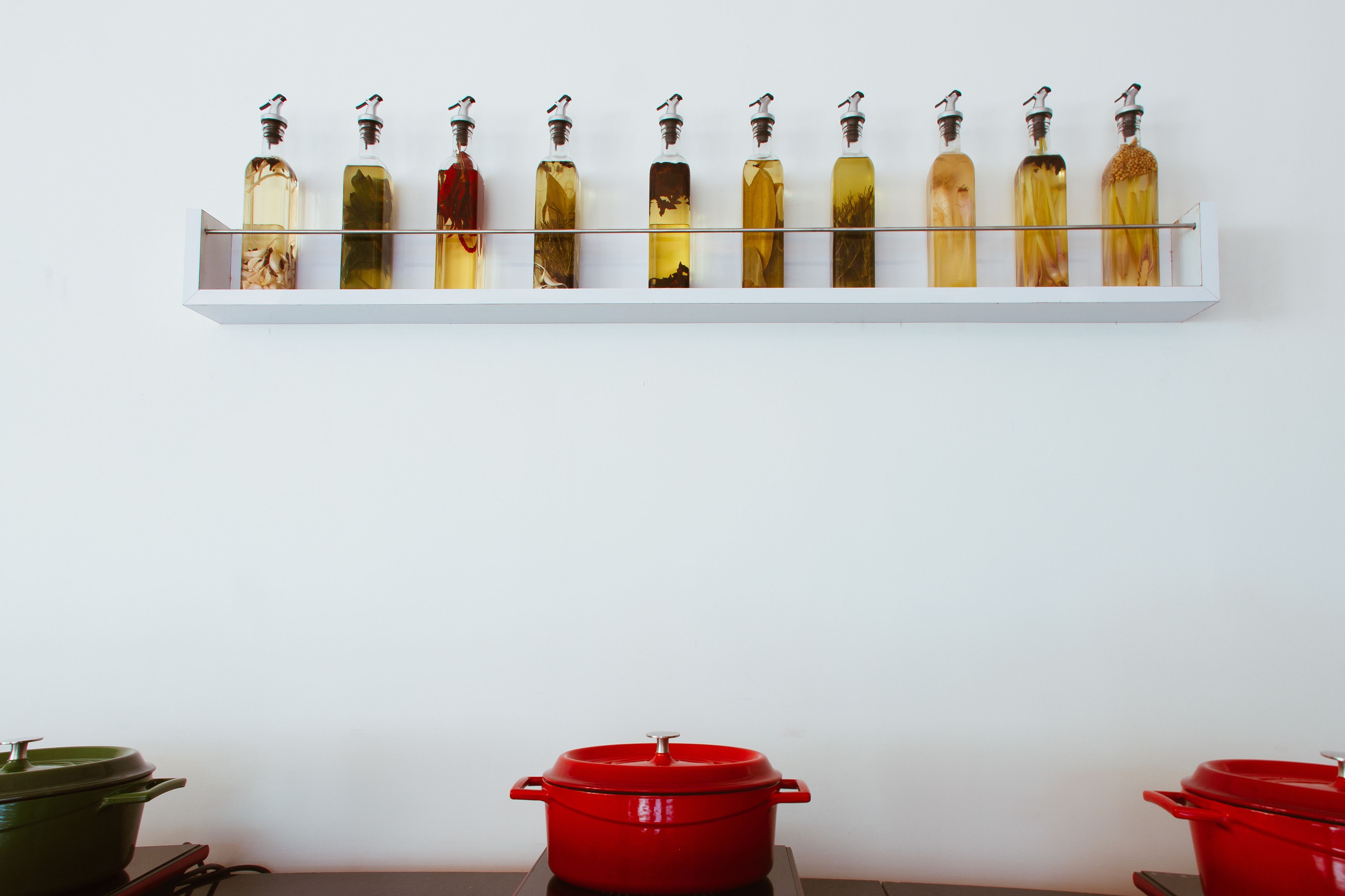 A kitchen with a white shelf holding various bottles and two red pots on the counter.