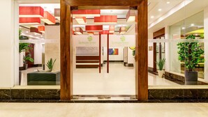 A hotel reception area with a modern design, featuring a reception desk, seating area, and potted plants.
