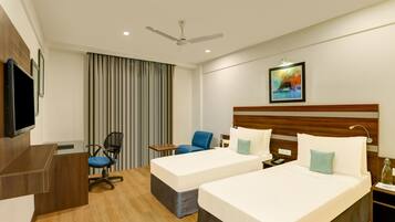 A hotel room with two beds, a desk, a chair, a television, and a ceiling fan.
