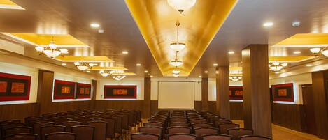 A conference room with rows of chairs, a projector screen, and multiple chandeliers.