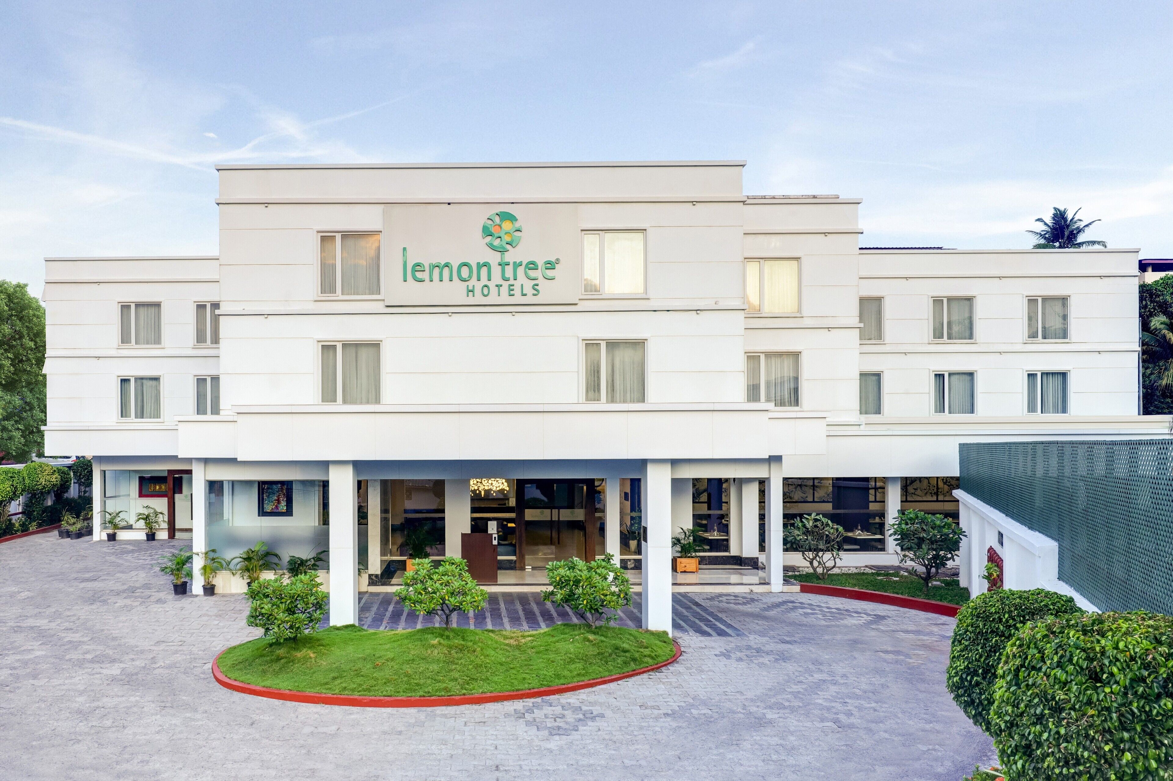 A modern hotel building with a prominent logo, a covered entrance, and a landscaped front yard.