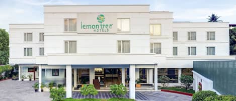 Un hotel moderno con un logotipo destacado, una entrada cubierta y un jardín delantero ajardinado.