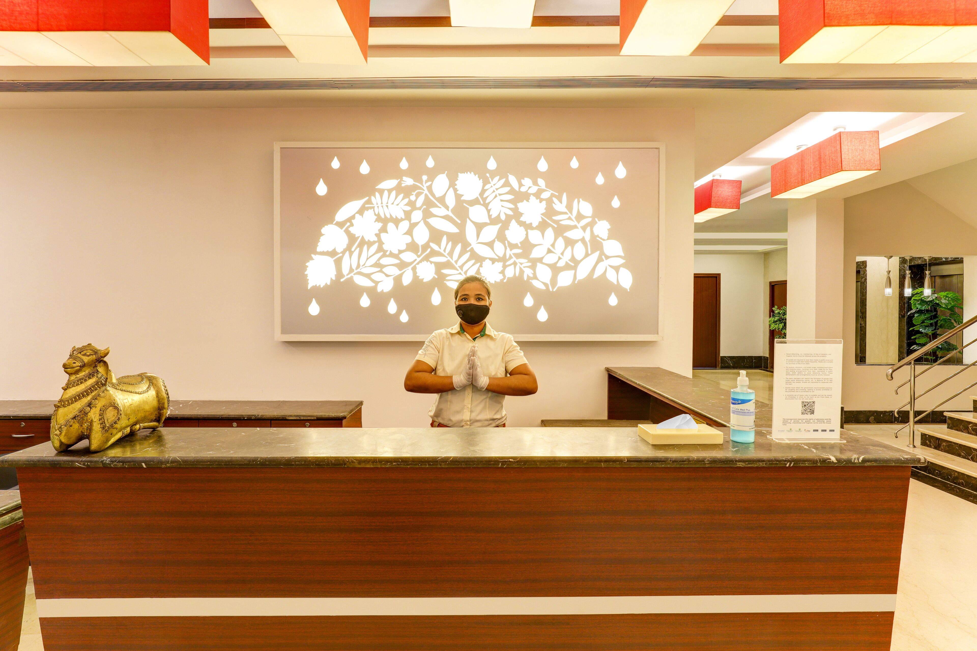A reception desk with a person standing behind it, a decorative golden horse, a floral wall art, and a sign with QR code.