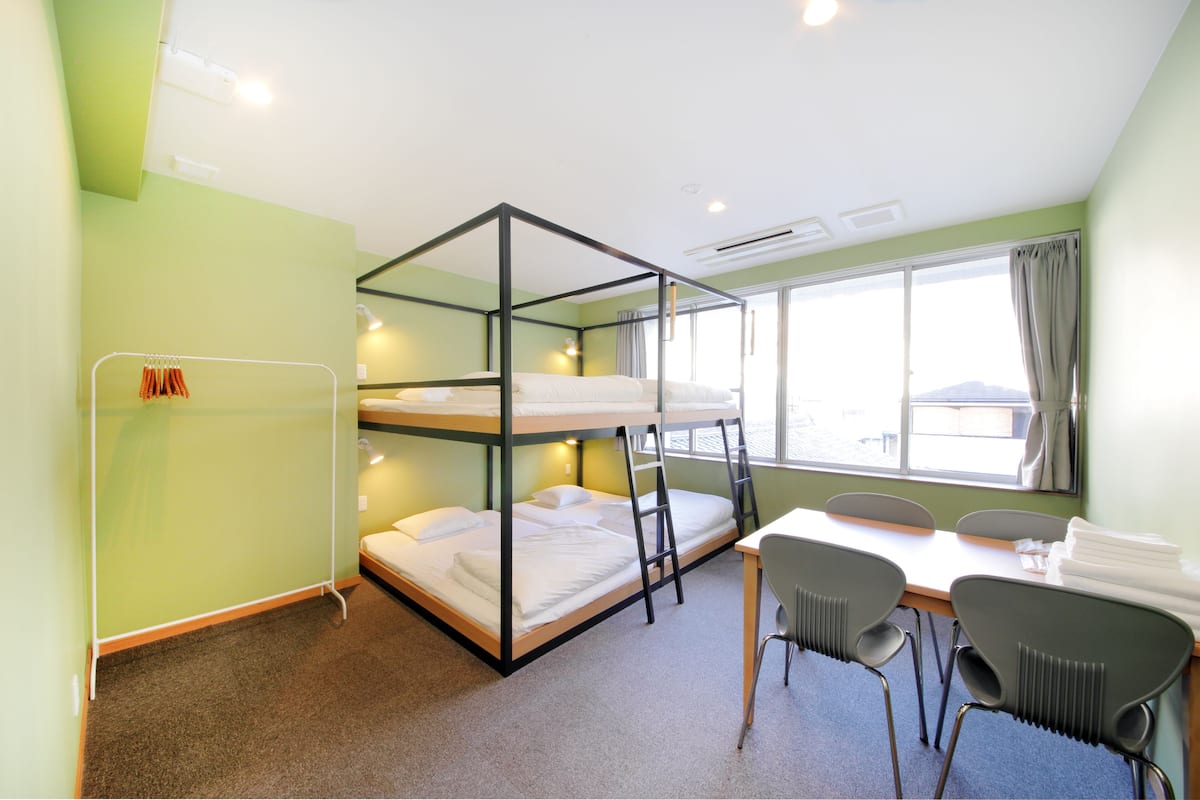 Une chambre avec un lit superposé, une table et des chaises, une fenêtre avec des rideaux et un porte-serviettes.