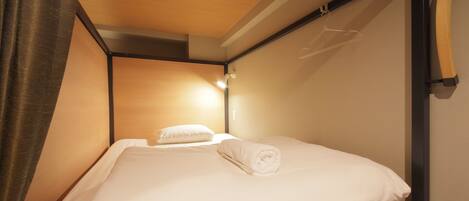 A single bed with a wooden frame and white bedding, a hanging light fixture, and a curtain partially covering the window.