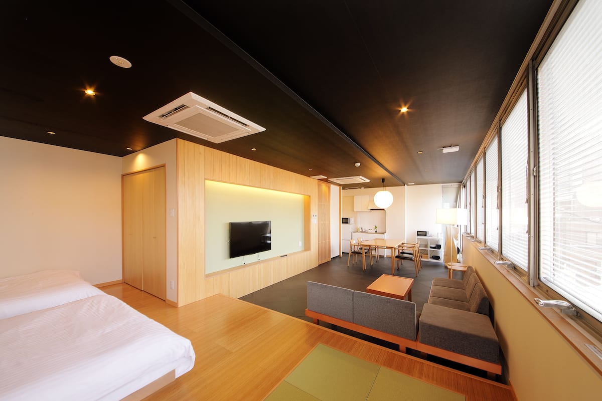Une chambre d’hôtel moderne avec un plancher en bois, un canapé, une télévision et un coin repas comprenant une table et des chaises.