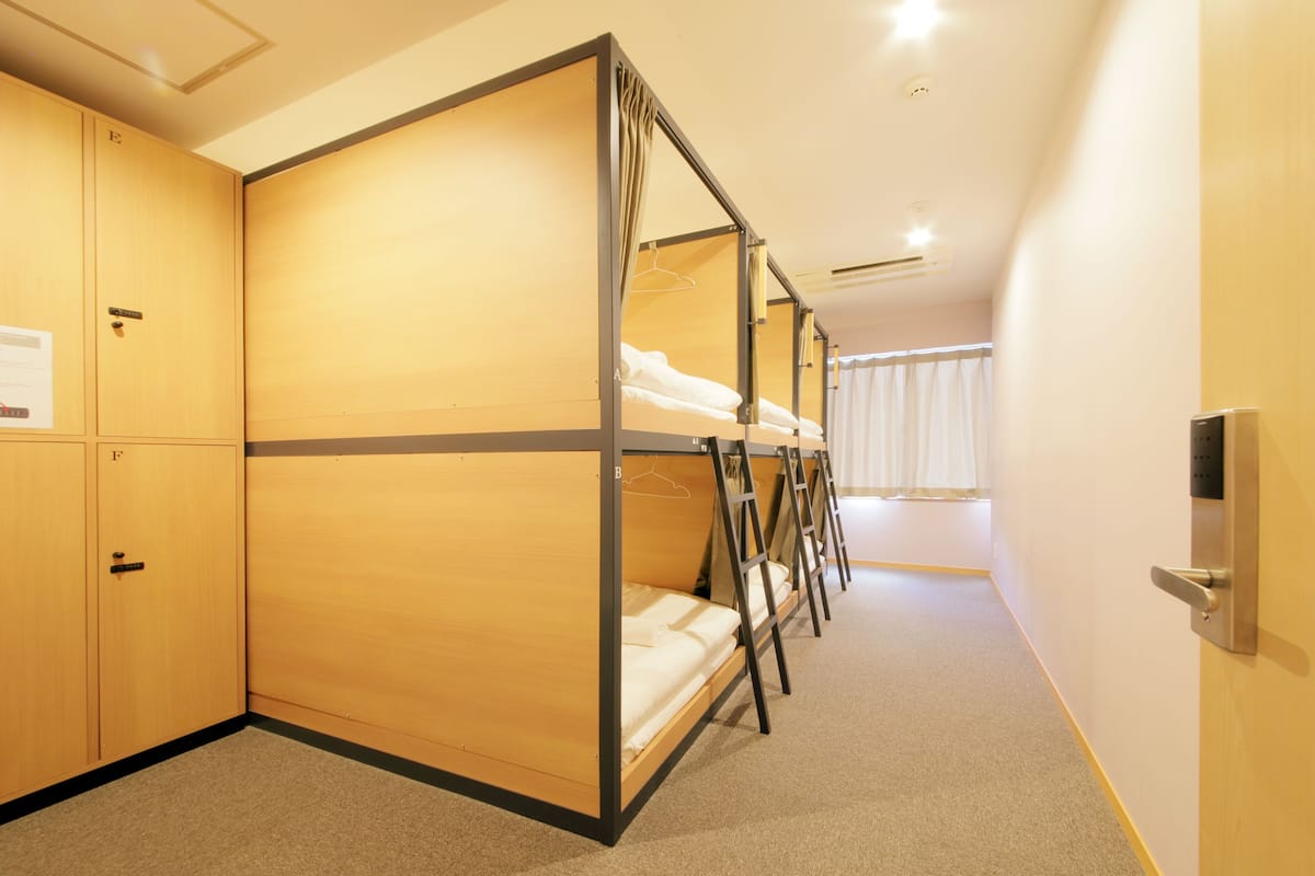 Une chambre d’hôtel avec des lits superposés, un sol recouvert de moquette, des murs en bois et une porte dotée d’une poignée.