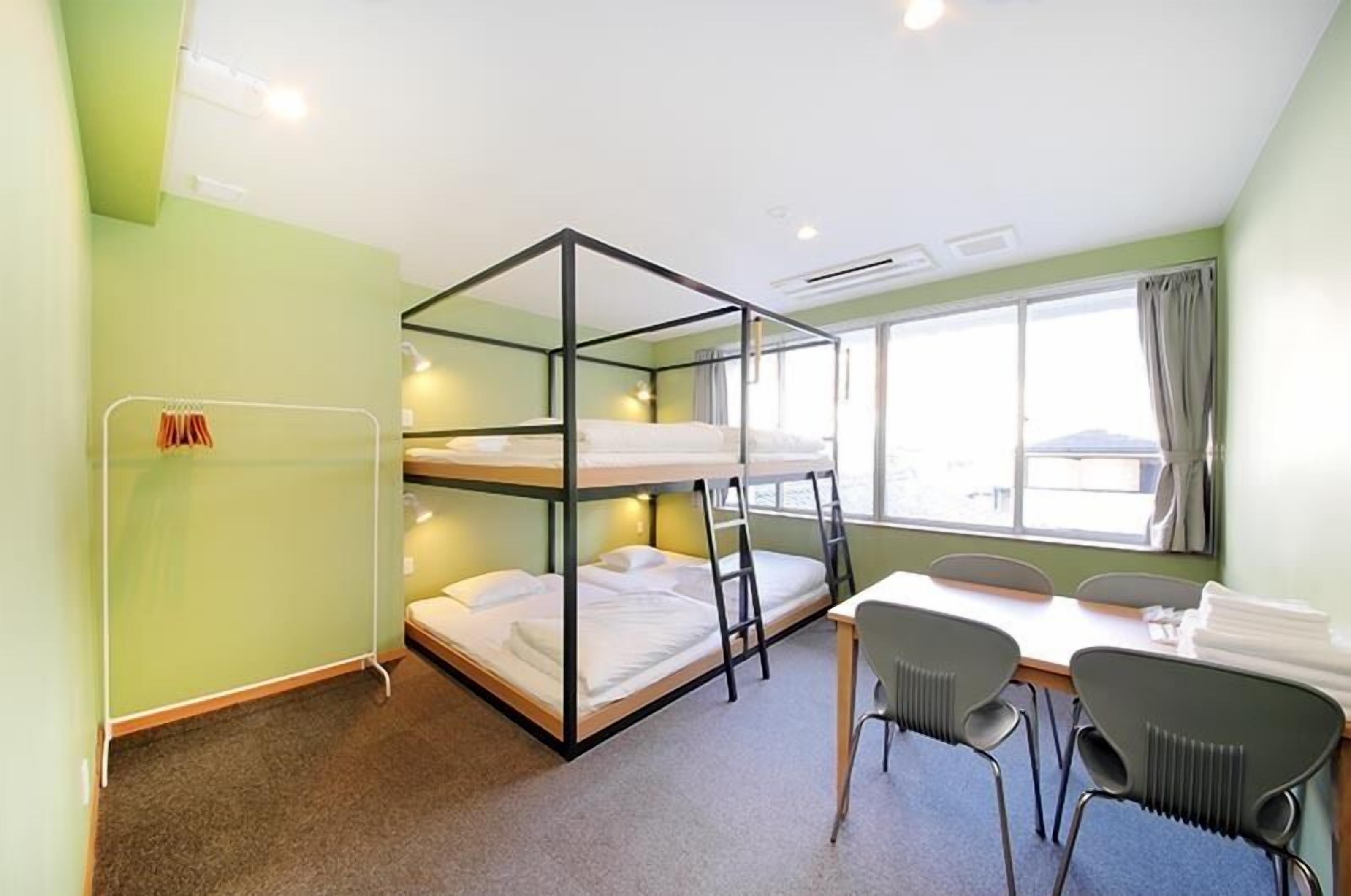 A bunk bed room with a table and chairs, a window with curtains, and a radiator.