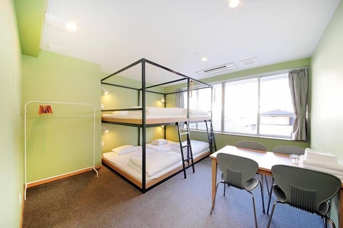 Une chambre avec un lit superposé, une table et des chaises, une fenêtre avec des rideaux et un radiateur.