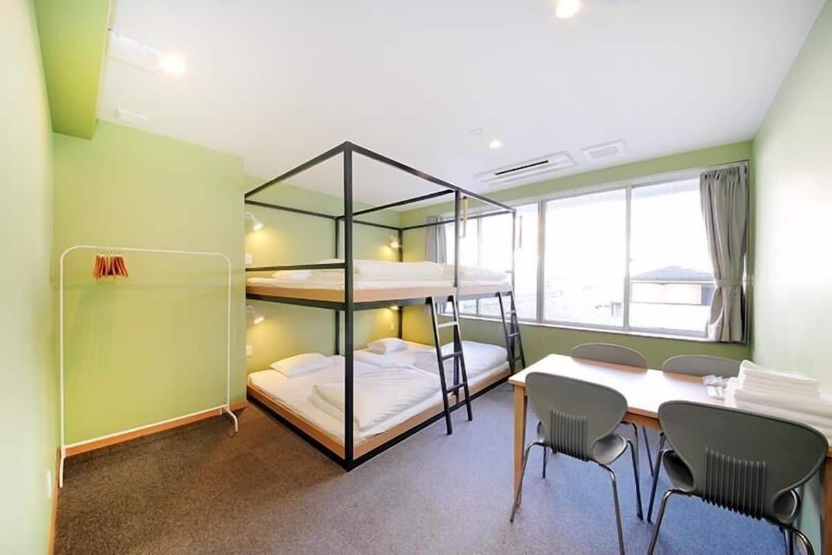 A bunk bed room with a table and chairs, a window with curtains, and a radiator.
