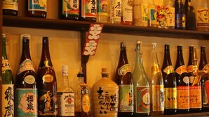 Un bar con estantes llenos de botellas y vasos, algunos con etiquetas japonesas.