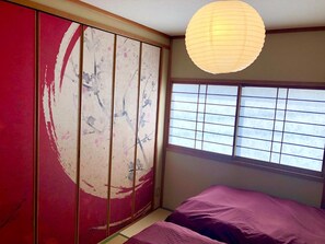Una habitación con un fusuma corredero, una cama con ropa de cama morada y un farol de papel colgando del techo.