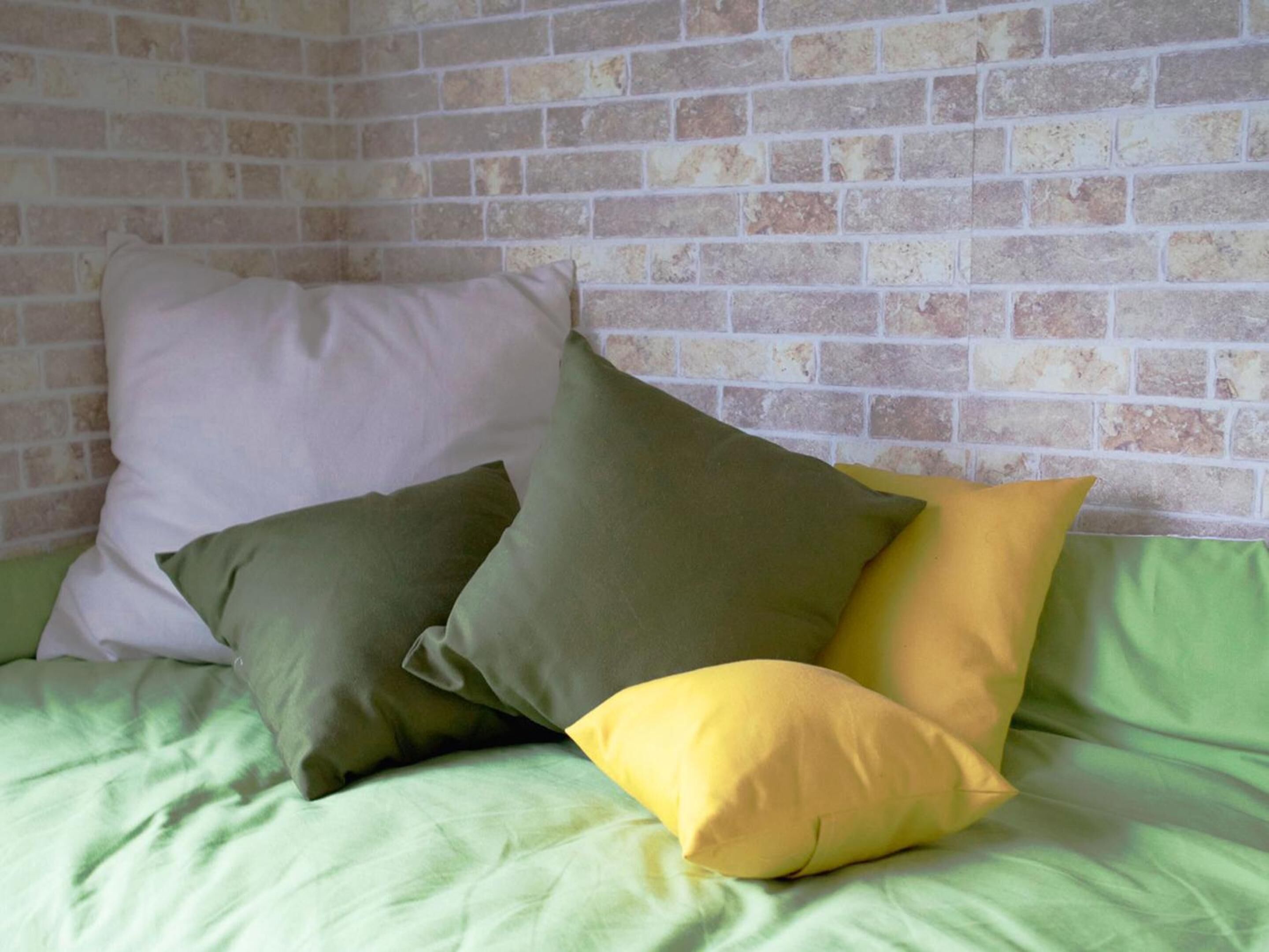 A bed with pillows in various colors against a brick wall.