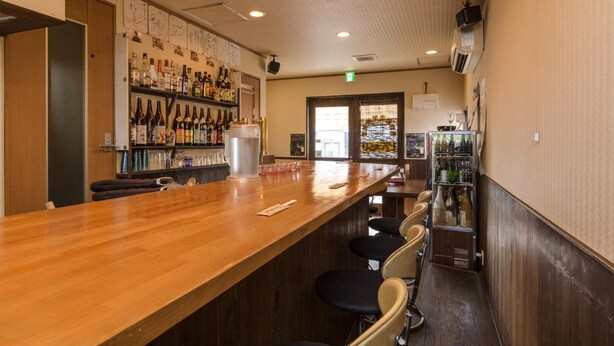 Zona de bar con mostrador de madera, taburetes y estantes llenos de botellas.