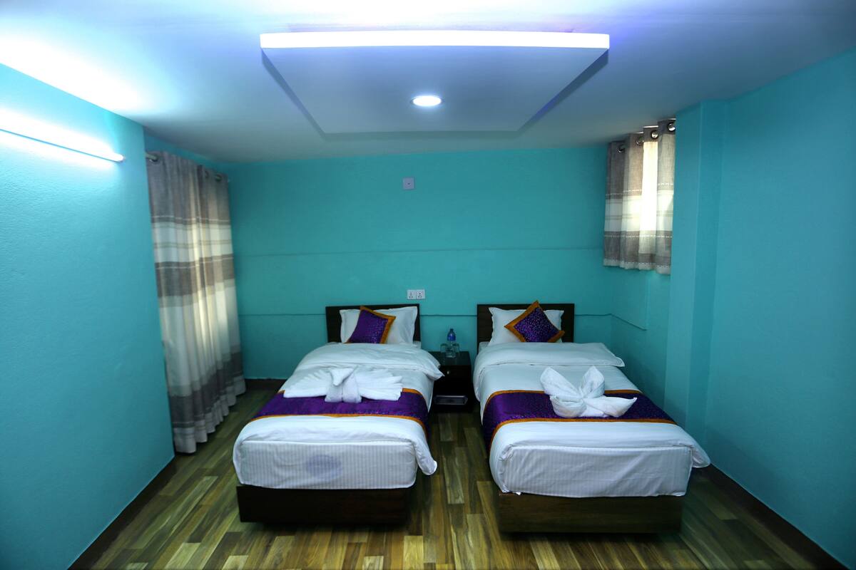 A room with two beds, teal walls, wooden flooring, and a ceiling light.