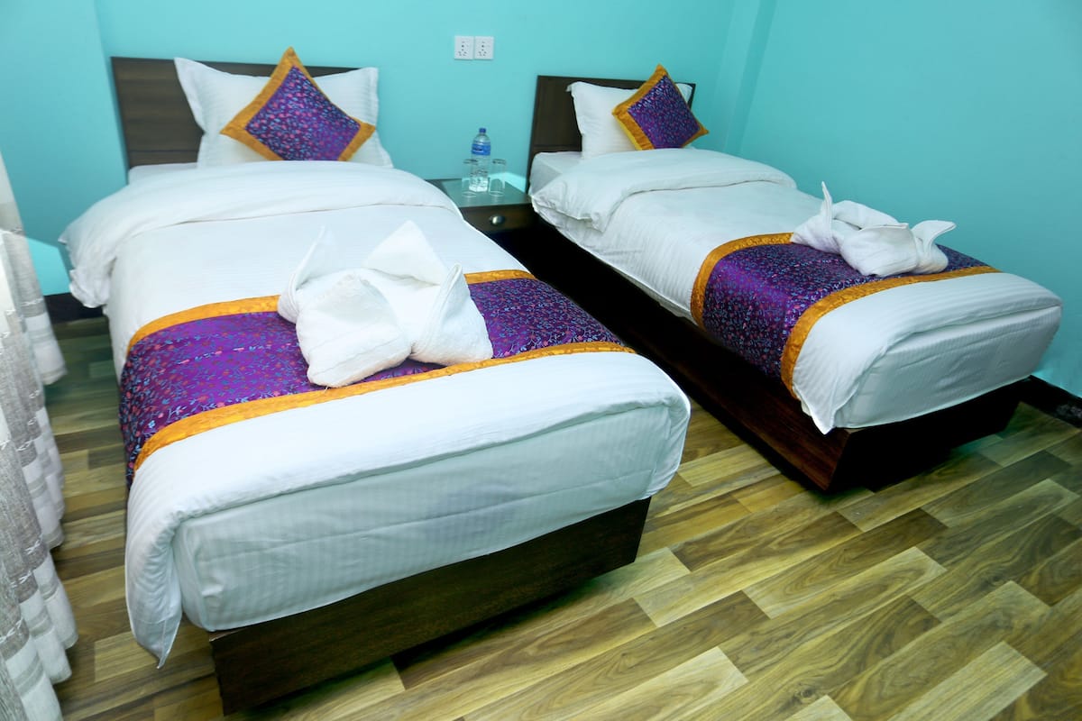 Two twin beds with white linens, purple and gold accents, and a wooden floor.