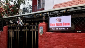 Entrada de hotel con una verja negra, un muro de ladrillo rojo y un letrero con el nombre y número de contacto del hotel.