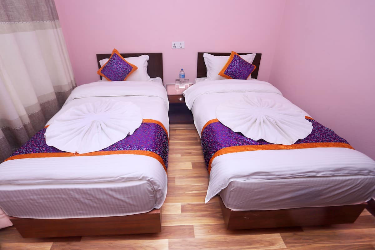 A twin room with two beds, each with a white duvet, purple and orange bedding, and a decorative white towel on the beds.