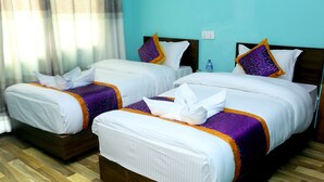 Dos camas individuales con ropa de cama blanca y detalles morados, cabeceros de madera y suelo de madera.
