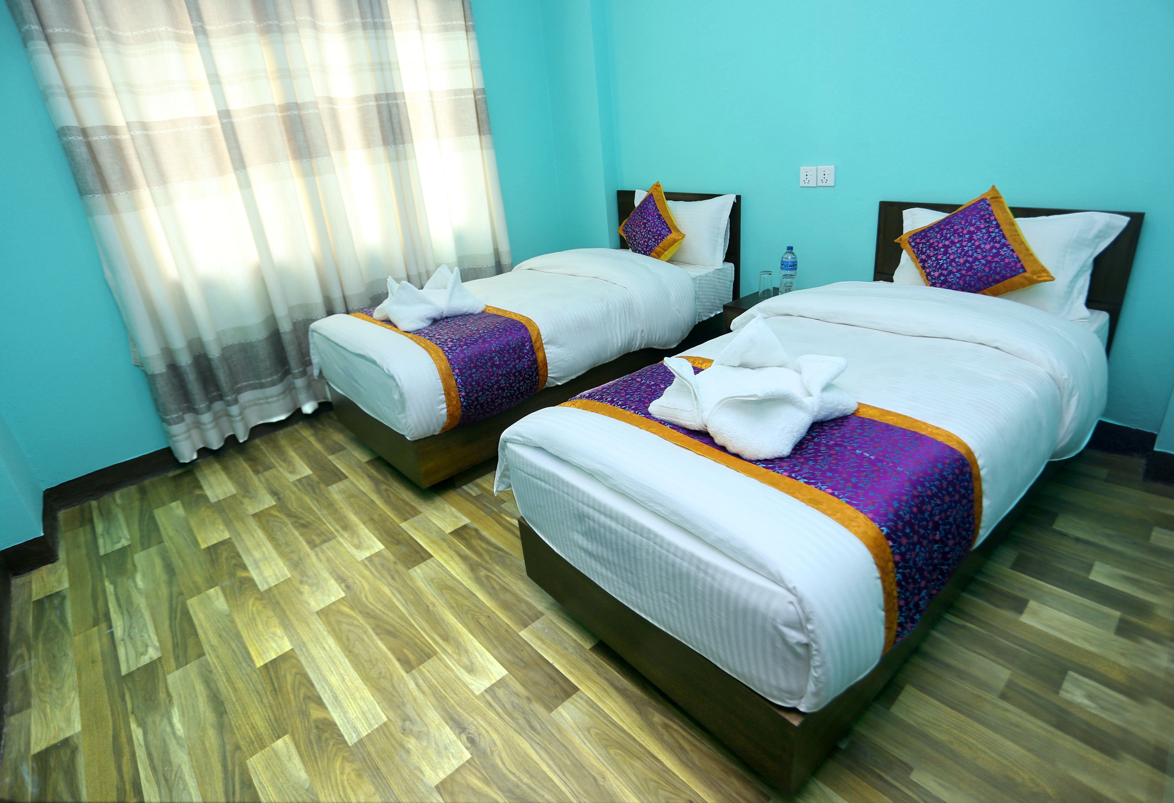 Habitación de hotel con dos camas, suelo de madera y ventana con cortinas.