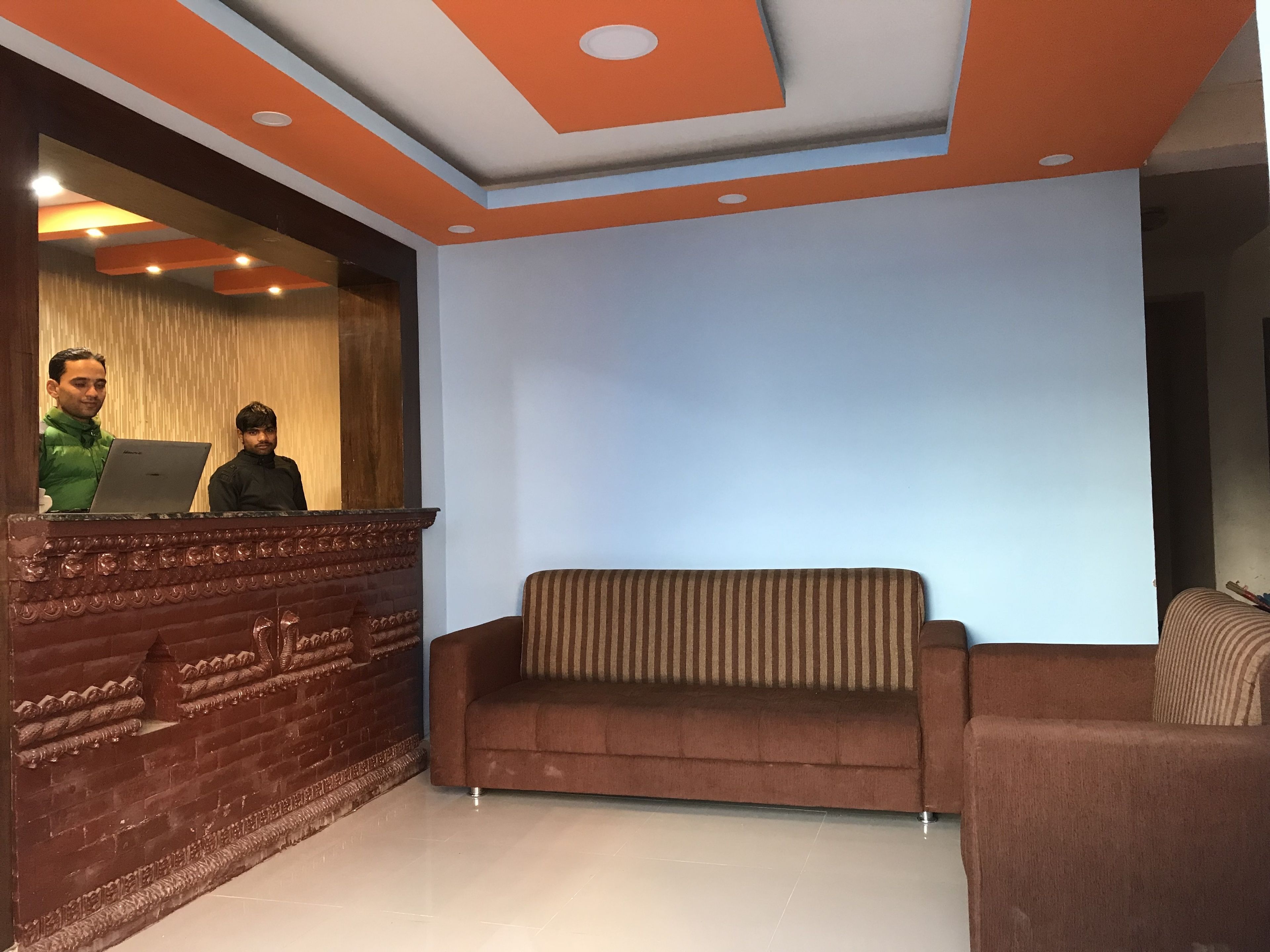 A reception area with a wooden reception desk, a brown sofa, and a striped cushion.