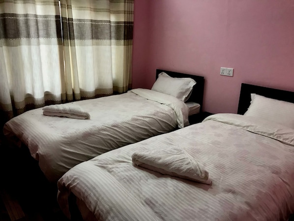 Un dormitori amb dos llits, una finestra amb cortines lleugeres i una paret rosa.