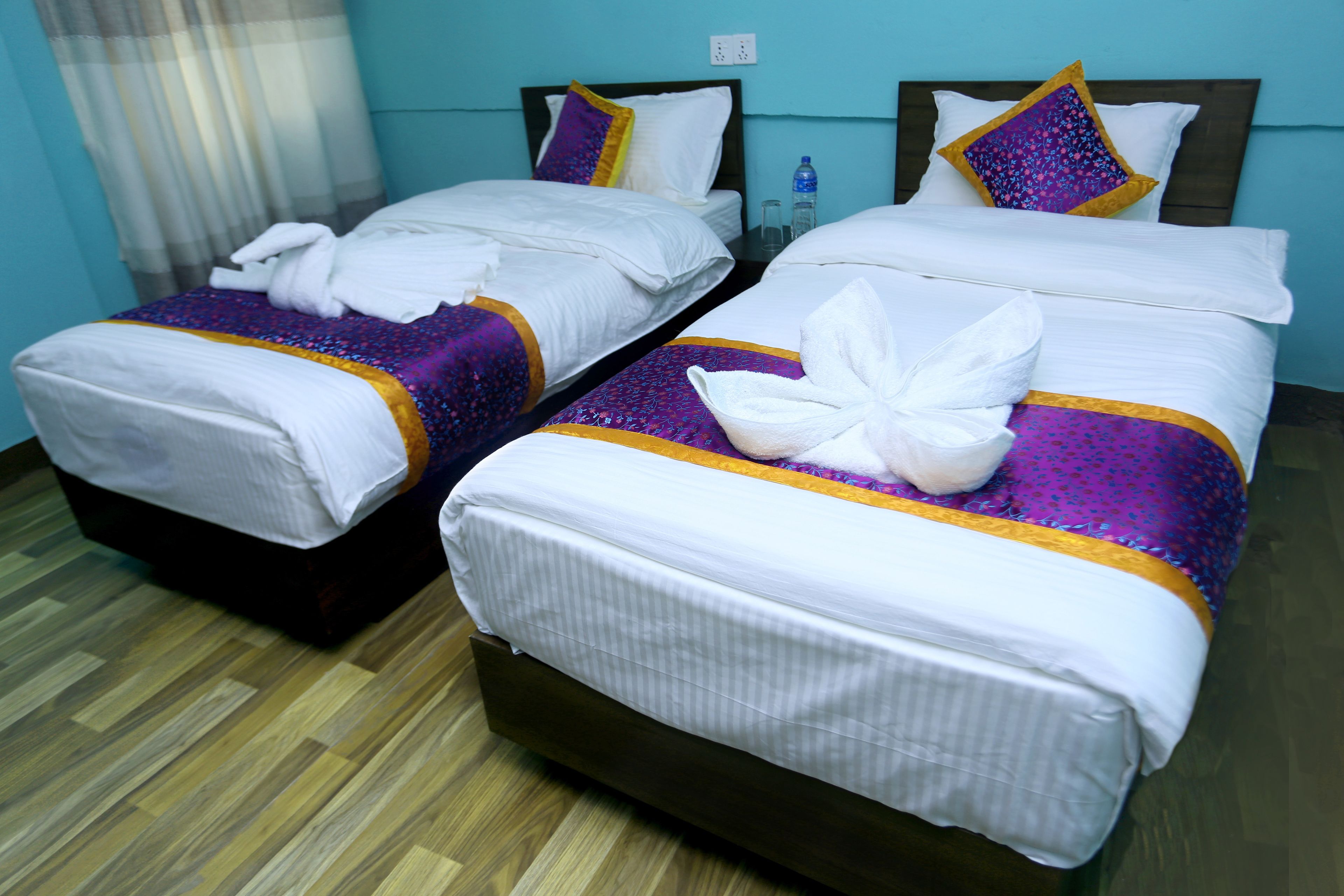 Two twin beds with white linens and purple accents, a wooden floor, and a blue wall.