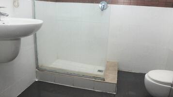 Un bany amb plat de dutxa de vidre, un lavabo i un vàter.