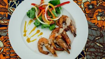 Un plato con camarones a la parrilla, ensalada y un chorrito de salsa.