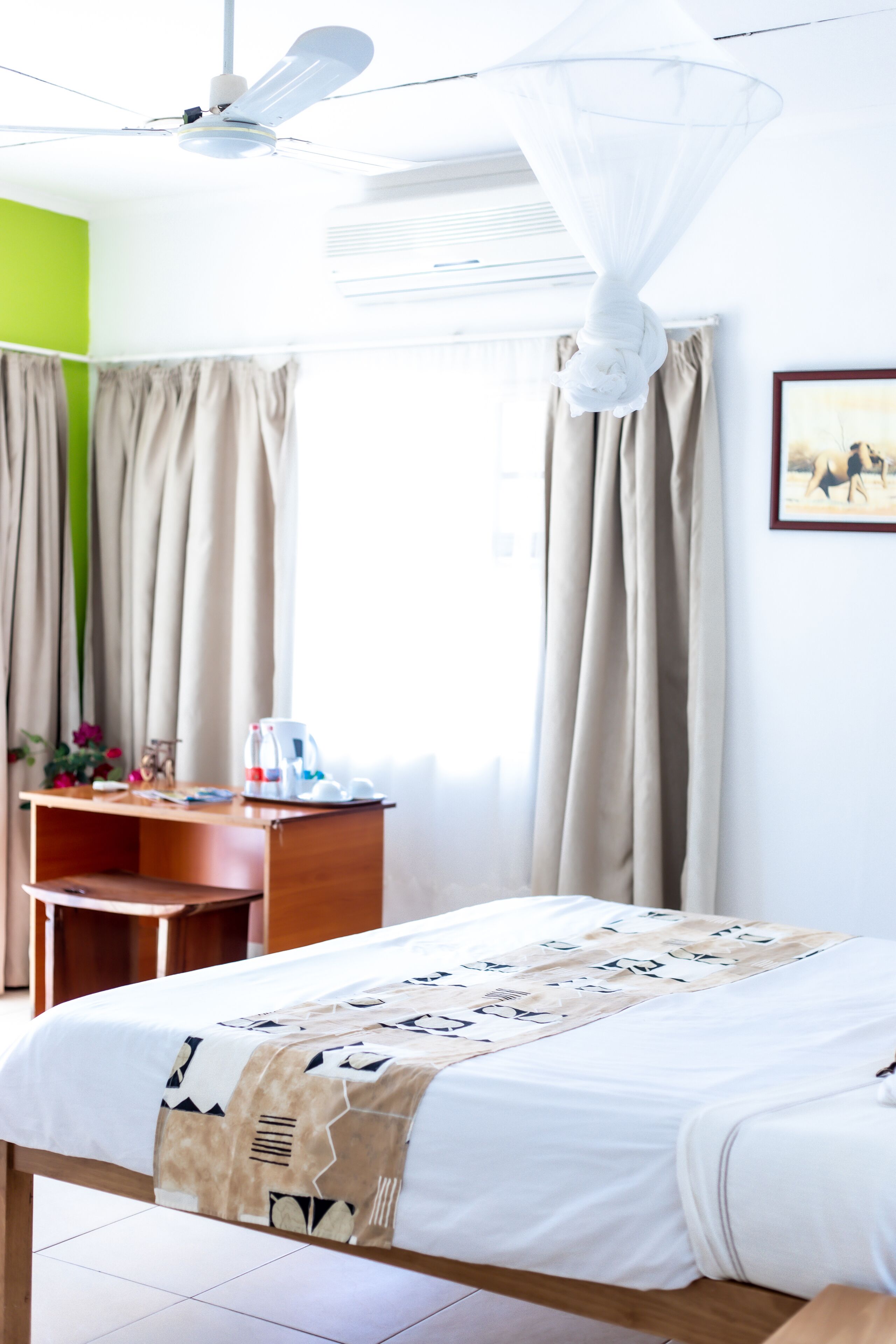 Una habitación de hotel con cama, escritorio, silla, ventana con cortinas y ventilador de techo.