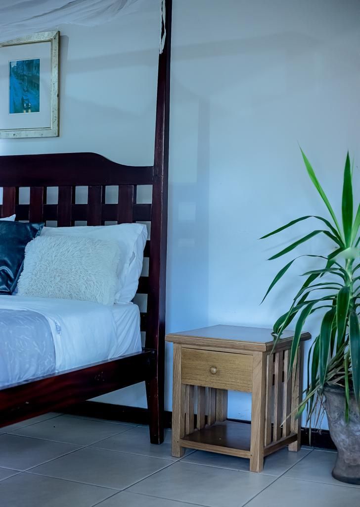 A bed with a wooden headboard, a bedside table with a drawer, and a potted plant.