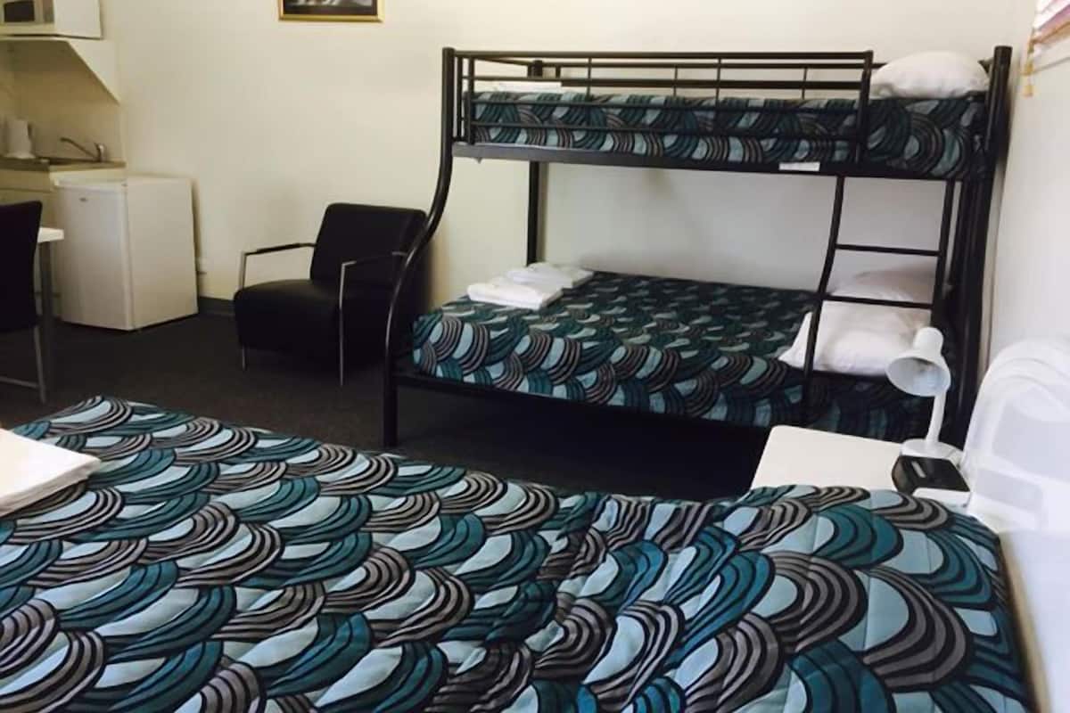 A bunk bed with patterned bedding, a desk with a computer, a chair, and a small refrigerator.