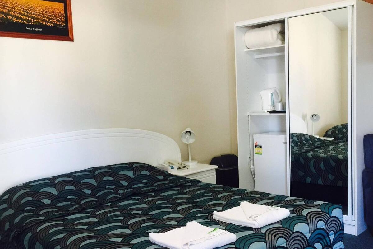 A hotel room with a bed, a wardrobe, a desk, and a chair.