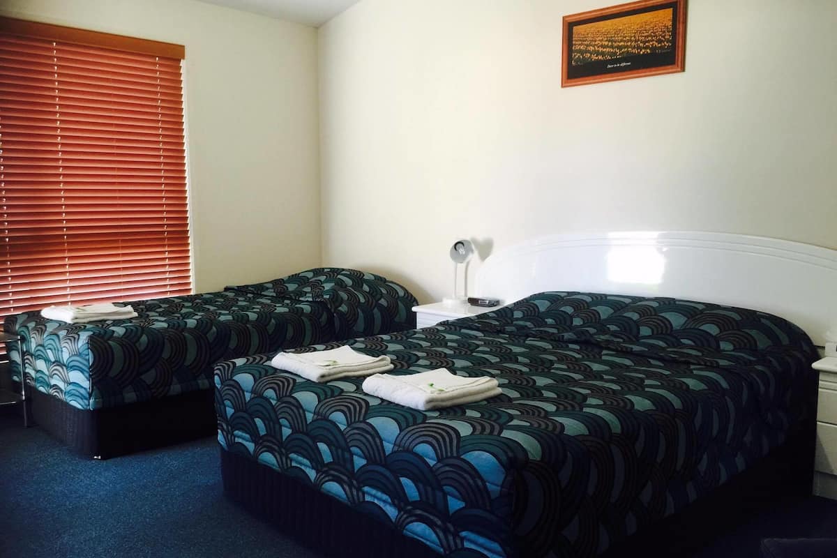 A hotel room with two beds, a bedside table with a lamp, and a framed quote on the wall.
