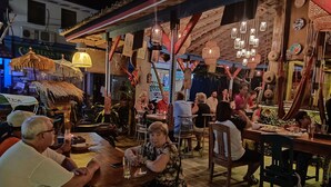 Un restaurante con mesas y sillas de madera, faroles colgantes y una estructura de techo de paja.