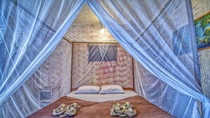 Una cama con mosquitera, una manta marrón y toallas con motivos florales.