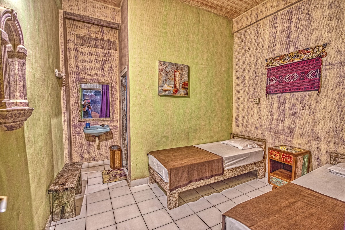 A room with two beds, a small sink, and a mirror.