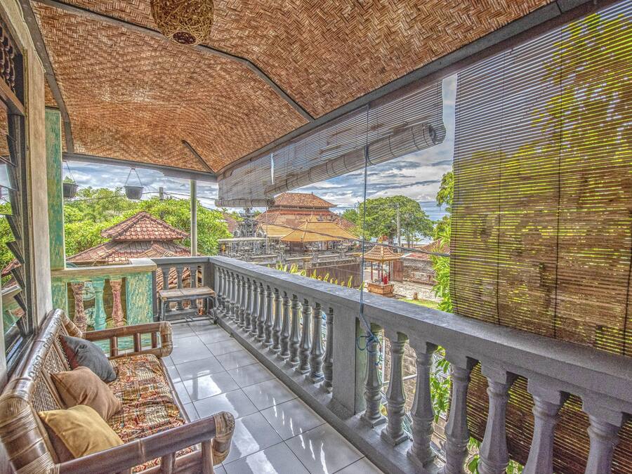 A balcony with a woven ceiling, a cushioned bench, and a view of traditional buildings.