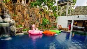 Una piscina con cascada, rocas y flamencos inflables.