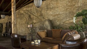 Un interior rústico con techo de madera, paredes de piedra, sofá de cuero, una mesa de centro y plantas colgantes.