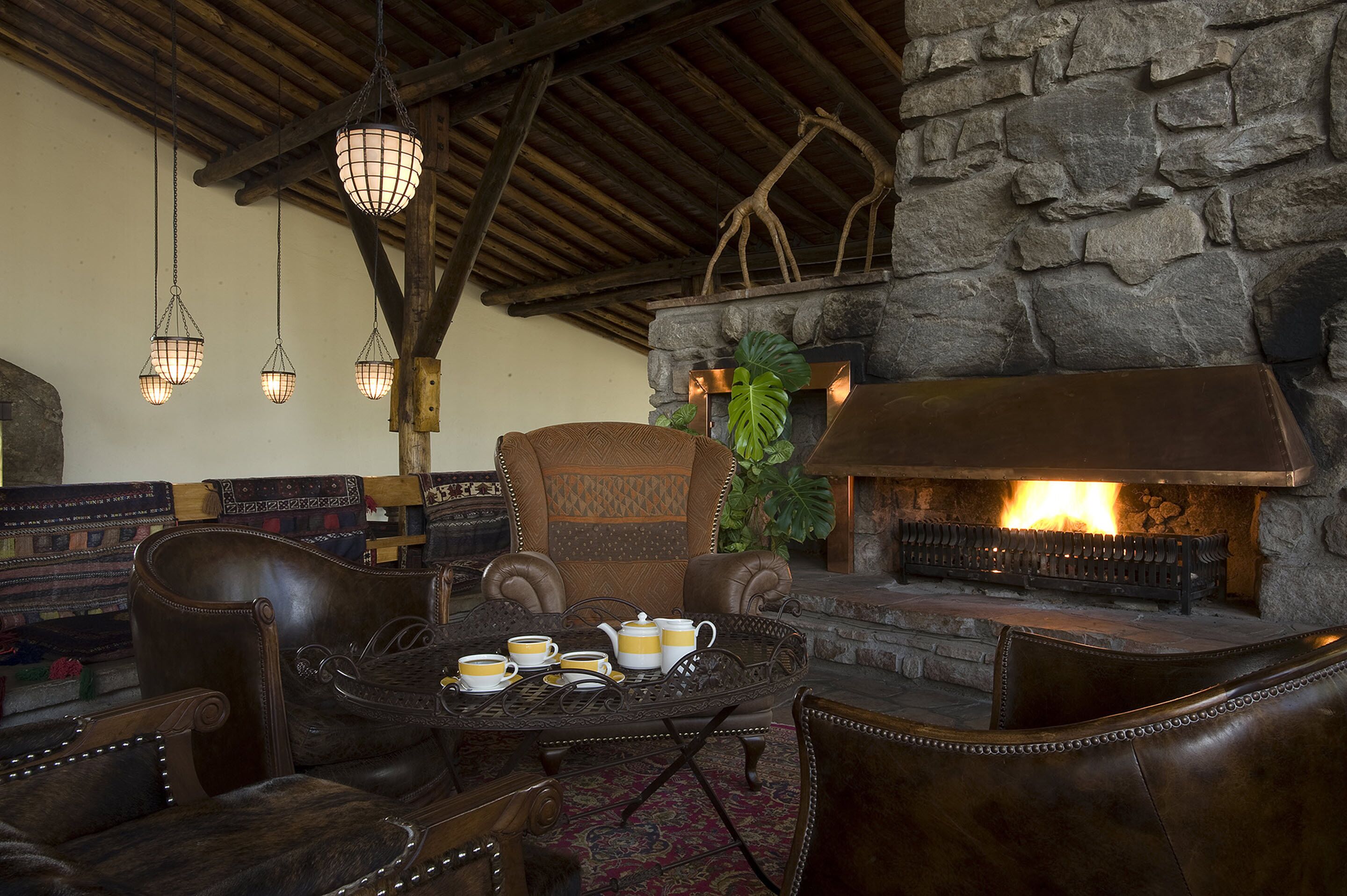 Un rincón lounge acogedor con mobiliario de cuero, chimenea de piedra y lámparas colgantes.