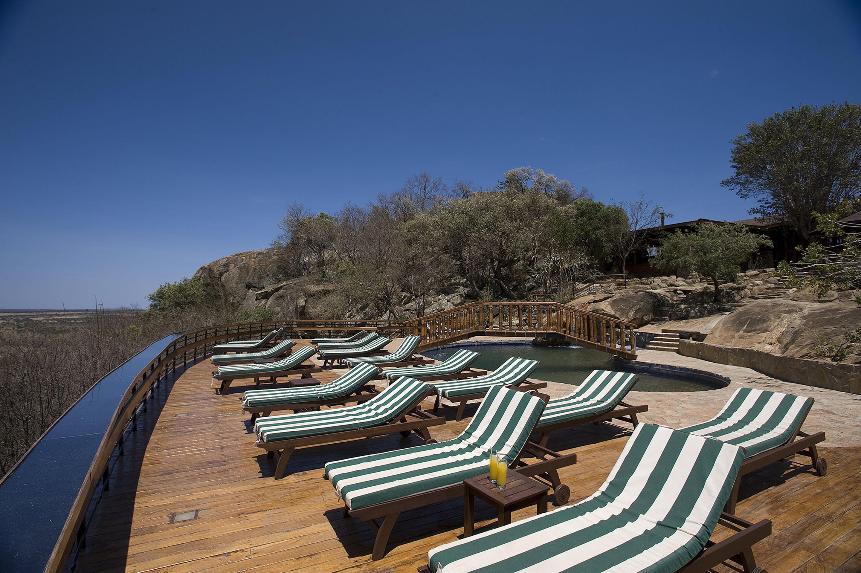 A wooden deck with lounge chairs and a pool, surrounded by natural landscape and trees.