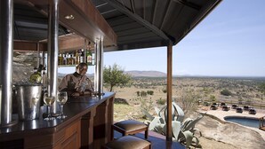 Un bar con vistas a un valle, una piscina y mesas al aire libre.